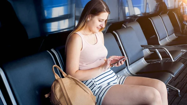 Молодая женщина сидит в аэропорту в ожидании рейса и просматривает интернет по мобильному телефону — стоковое фото