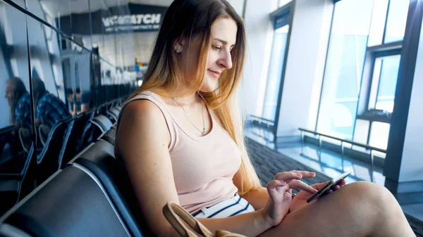 Portrait of beautiful smiling woman with smartphone waiting for flight in airport — Stock Photo, Image