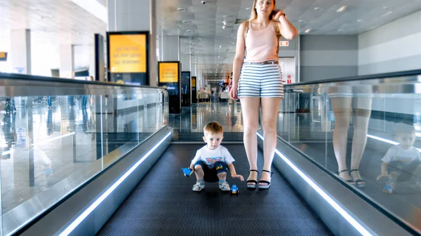 Young mother with toddler son standing on moving walkway at big modern airport — Stock Photo, Image