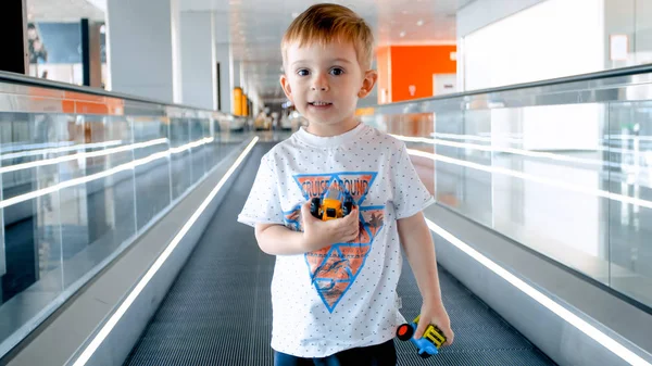 Retrato de lindo niño sonriente de pie en la pasarela en movimiento en la terminal del aeropuerto — Foto de Stock