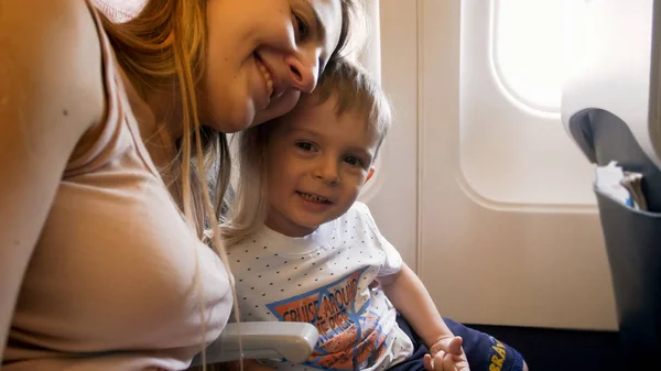 Yolcu jet uçağında oturan küçük oğlu ile mutlu kucaklayan anne portresi — Stok fotoğraf