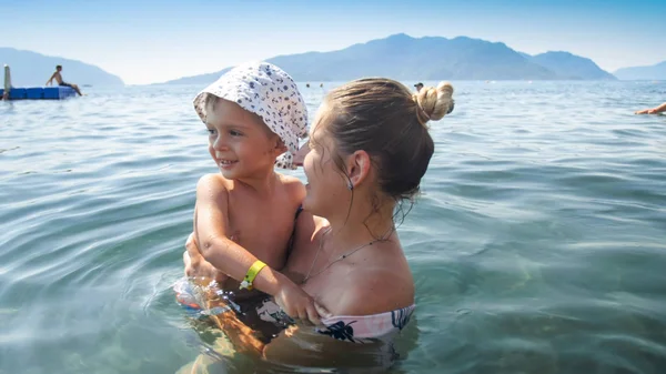 Nahaufnahme Porträt einer jungen Frau, die ihren kleinen Sohn beim Schwimmen im Meer hält und umarmt — Stockfoto