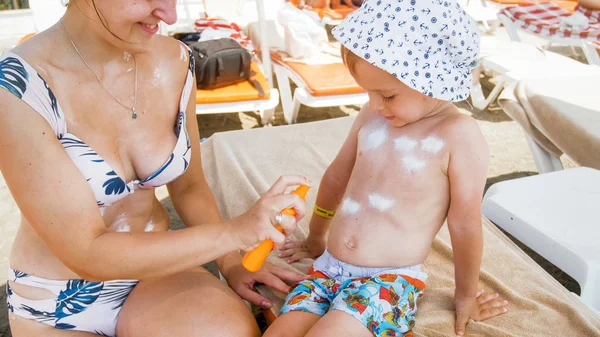 Jonge moeder beschermt haar peuter zoon tegen aggresieve zon Uv licht op het strand — Stockfoto