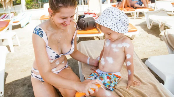 Junge Mutter schützt ihren kleinen Sohn vor aggressivem Sonnenlicht am Meeresstrand — Stockfoto