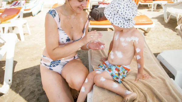 Mały maluch chłopiec z matką za pomocą balsamu do opalania na plaży morskiej — Zdjęcie stockowe