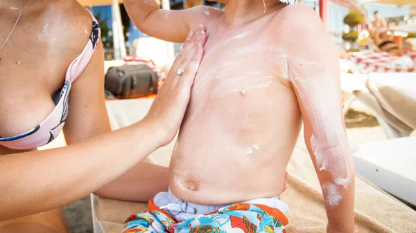 Immagine ravvicinata della giovane madre che protegge il suo bambino dalla luce UV dannosa sulla spiaggia durante la giornata di sole — Foto Stock