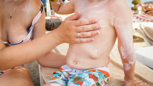 Little toddler boy with mother using sunblock lotion on sea beach — Stock Photo, Image