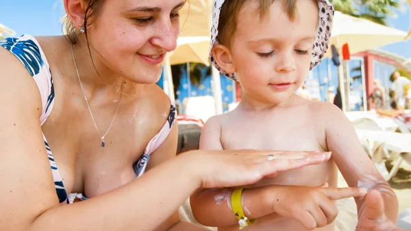 Closeup photo of young woman with her little child relaxing on beach and applying sunscreen lotion — Stock Photo, Image