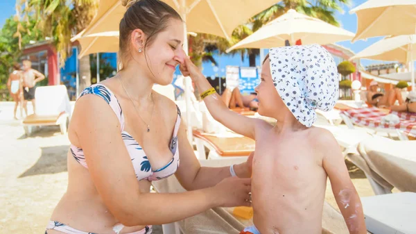 Happy young mother with her little toddler sun having fun while applying sunscreen lotion on the sea beach at sunny summer day — Stock Photo, Image