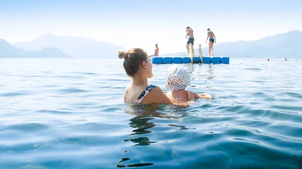 Mujer joven con su pequeño hijo nadando hasta el muelle flotante en el mar —  Fotos de Stock