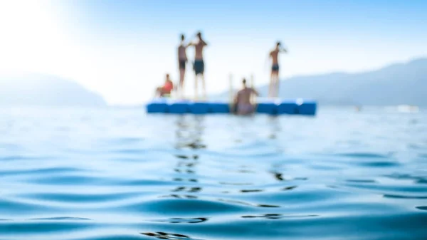 Blurred photo of group of people relaxing on floating pier at calm sea — Stock Photo, Image