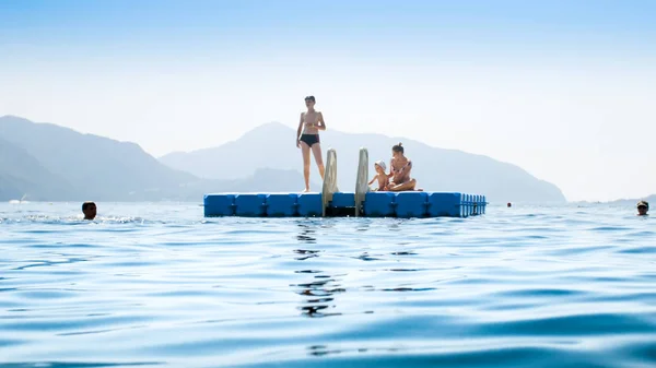 Ευτυχισμένοι νέοι άνθρωποι στέκονται σε πλωτή προβλήτα στη θάλασσα σε φωτεινή ηλιόλουστη μέρα — Φωτογραφία Αρχείου