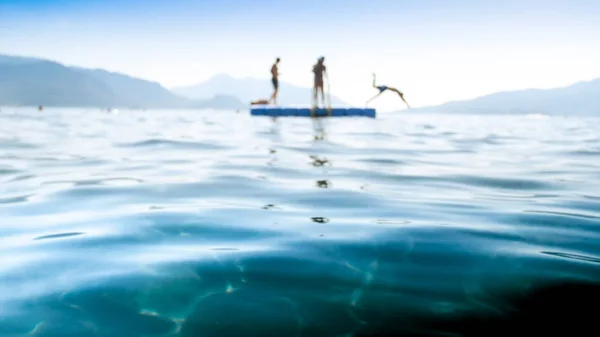 Imagen borrosa de hombres jóvenes saltando desde un pontón flotante en el mar —  Fotos de Stock