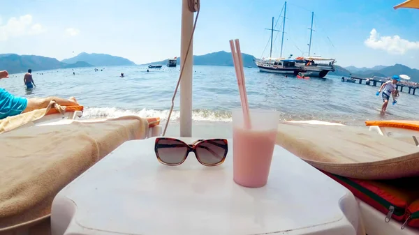 Κοντινό πλάνο γυαλιών ηλίου και κοκτέιλ στο τραπέζι μεταξύ ξαπλώστρες στην παραλία — Φωτογραφία Αρχείου