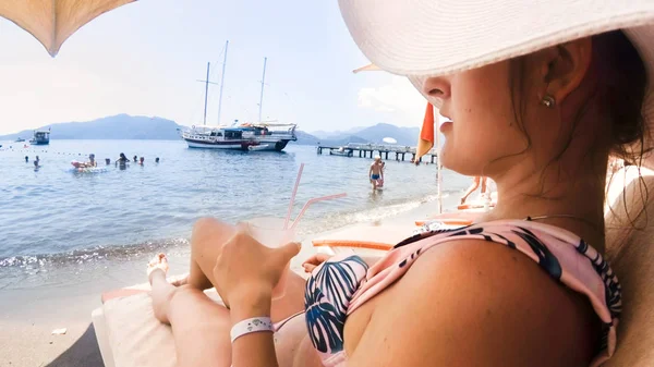 Image of beautiful young woman in swimsuit and hat relaxing on sunbed at sea beach — Stock Photo, Image