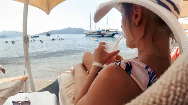 Сексуальна молода жінка лежить з коктейлем під сонячною парасолькою на морському пляжі — стокове фото