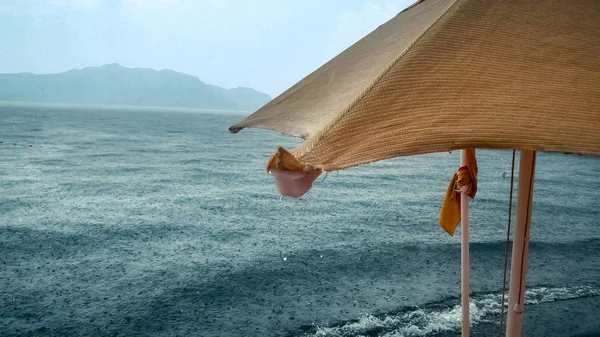 Closeup image of water droplets falling from parasol during rain at sea beach — Stock Photo, Image