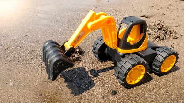 玩具挖掘机在沙滩上挖湿沙的特写照片。建筑与建筑的概念. — 图库照片