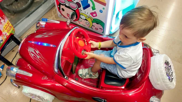 Pequeño niño divirtiéndose en el parque de diversiones. Niño cabalgando en insertar moneda coche eléctrico en el centro comercial — Foto de Stock