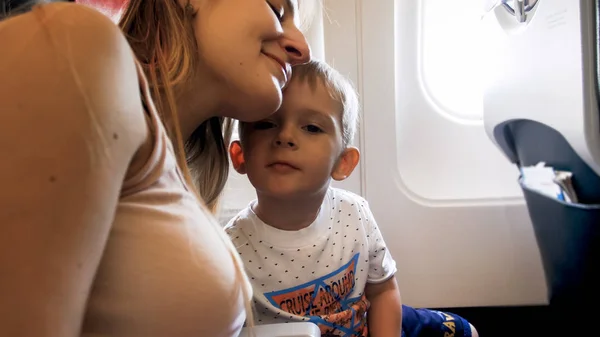 Nahaufnahme Porträt einer lächelnden Mutter, die ihren kleinen Sohn während des Fluges im Flugzeug umarmt — Stockfoto