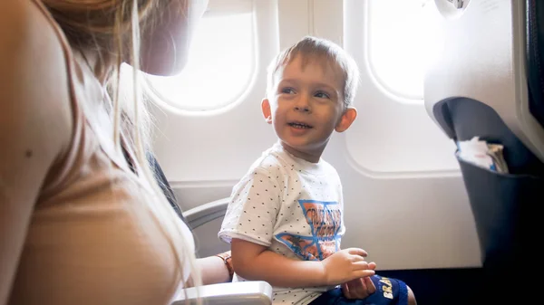 Porträt eines fröhlich lächelnden Kleinkindes, das im Flugzeug sitzt und Mutter ansieht — Stockfoto