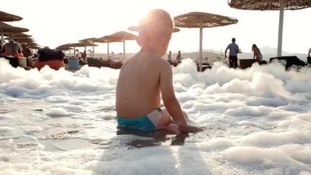 4k video de niño jugando en espuma después de la fiesta de espuma en la playa del mar — Vídeos de Stock