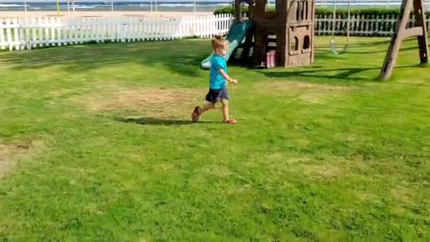 4K πλάνα από αξιολάτρευτο ευτυχισμένο αγόρι τρέξιμο και το παιχνίδι με μπάλα στο γρασίδι στην παιδική χαρά — Αρχείο Βίντεο