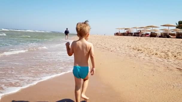 4k video de niño pequeño caminando en la playa de arena en el mar — Vídeo de stock