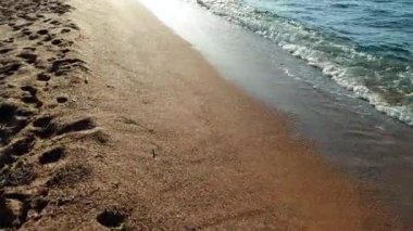 Gün batımında sahilde sakin deniz dalgaları ve kum üzerinde uçan kamera 4k video