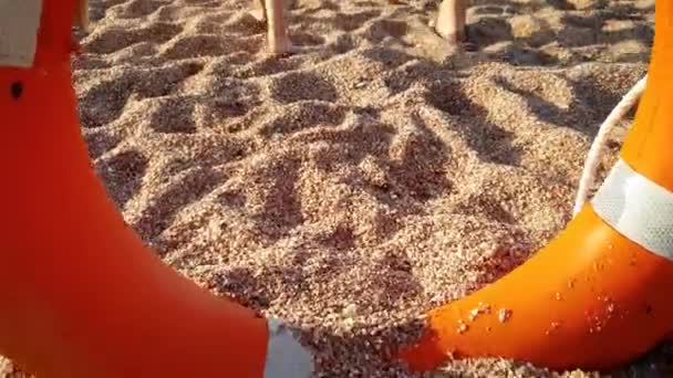 4K video av kamera flyger genom livräddande boj och visar ung mamma med liten pojke gå på stranden mot havet — Stockvideo