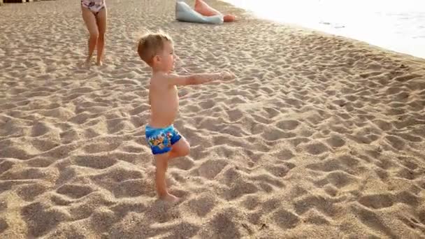 4k video o veselém batole a mladé matce, která hraje s míčem na mořské pláži při západu slunce