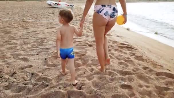 4k video de hermosa mujer joven con su niño de 3 años de edad niño caminando en la playa al atardecer — Vídeos de Stock