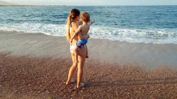 4k vídeo de jovem mulher abraçando sua pequena chiild na praia ao pôr do sol — Vídeo de Stock