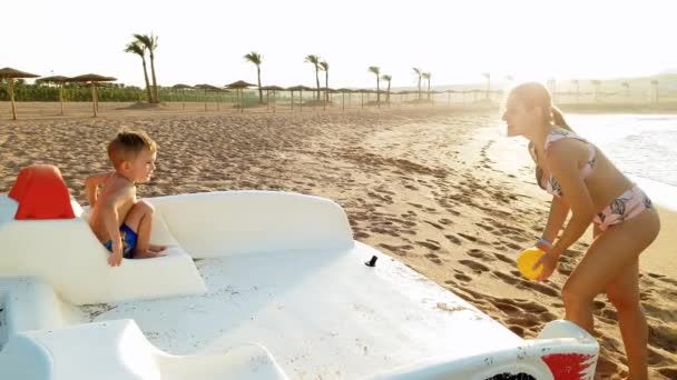 4k vídeo de menino feliz brincando com sua mãe na praia do mar ao pôr do sol. FAmily jogar bola em férias de verão — Vídeo de Stock