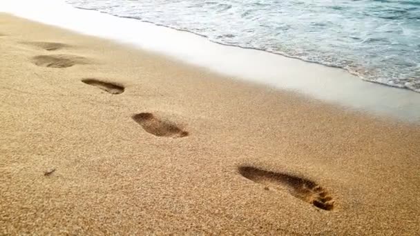 4k vídeo of sea waves rolling over footprints on wet sand on the beach at sunset light — Vídeo de Stock