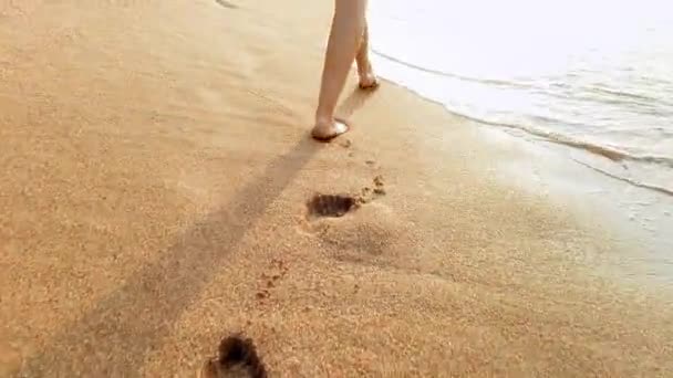 4k vídeo de sexy pés femininos andando na areia molhada e ondas do mar ao pôr do sol luz — Vídeo de Stock