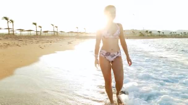 4k video van mooie lachende vrouw in bikini wandelen op het strand bij zonsondergang — Stockvideo