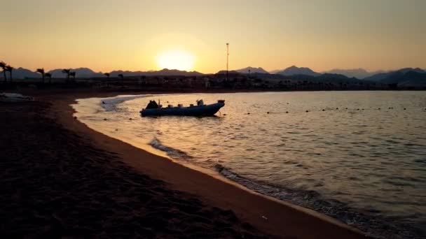 4k video de lancha motora inflable flotando en el mar junto a la playa de arena en la luz del atardecer — Vídeos de Stock