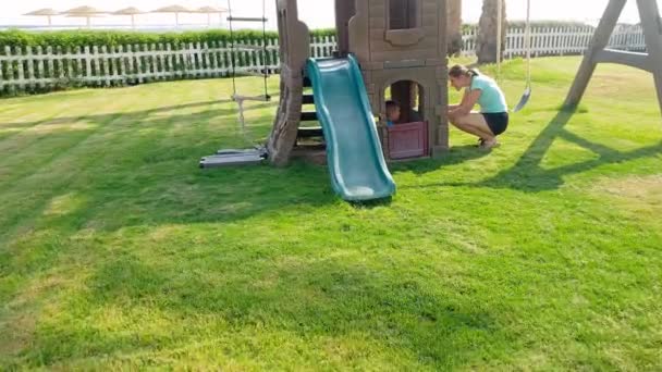 4k відео чарівного хлопчика, який грає на ігровому майданчику зі своєю матір'ю і ховається в замку пластикової іграшки — стокове відео
