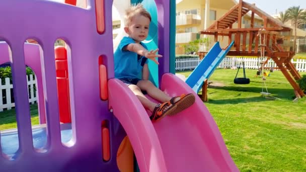 4k imagens de alegre sorridente criança menino montando na corrediça em crianças playground no parque — Vídeo de Stock