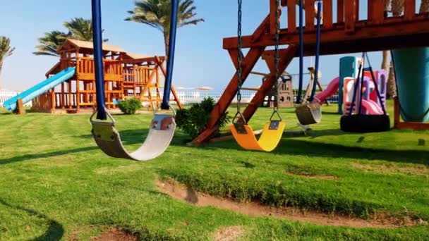 4k close seup footage of empty swing on the children playground next to the sea beach — стоковое видео