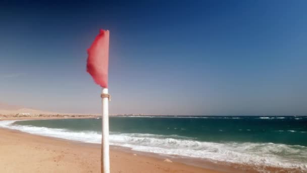 Βίντεο 4K με φτερούγισμα κόκκινη σημαία στη θυελλώδη ημέρα στη θάλασσα παραλία — Αρχείο Βίντεο