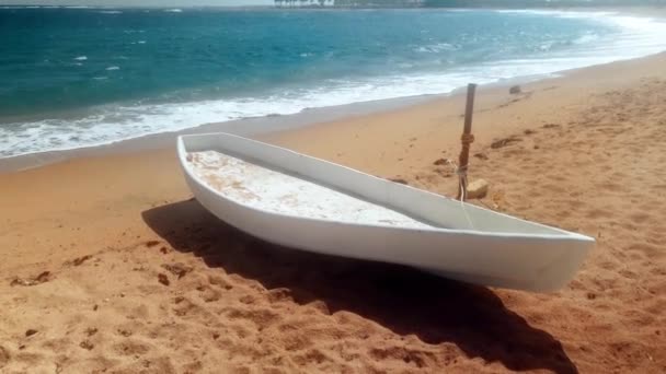4k видео белой деревянной лодки для рыбалки, лежащей на морском пляже в солнечный ветреный день — стоковое видео
