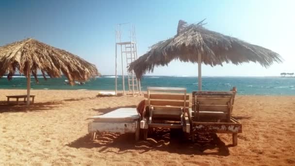 4K πλάνα από εγκαταλελειμμένη θάλασσα παραλία με ξύλινες ξαπλώστρες και ομπρέλες σε θυελλώδη ημέρα — Αρχείο Βίντεο