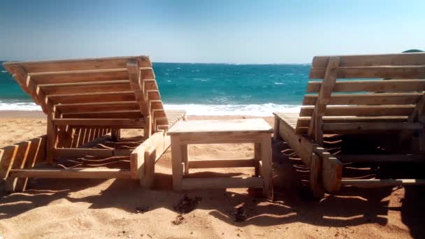 4k videó két fából készült napozóágyak és a kis asztal az elhagyott tengeri strandon — Stock videók