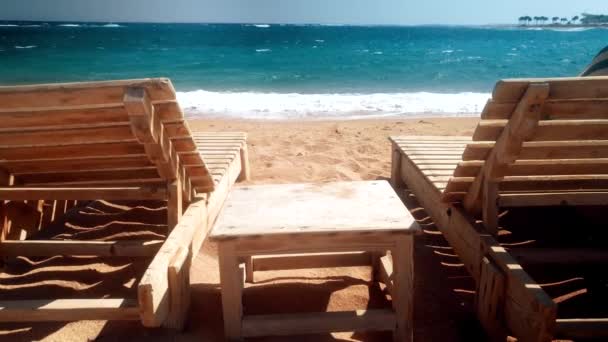 4k видео двух деревянных шезлонгов на пляже. Высокие волны катятся по побережью — стоковое видео