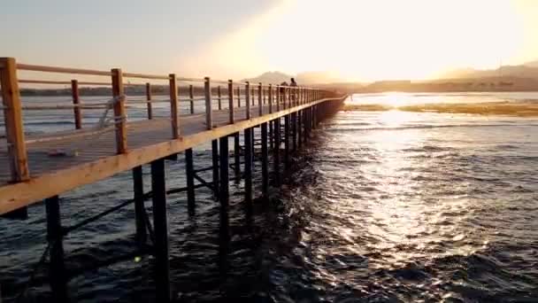 4k felvételt a gyönyörű, hosszú, fából készült mólón a tengerben naplementekor — Stock videók