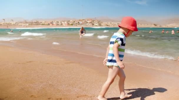 4k slow motion vídeo of cheerful 3 years old toddler boy playing on the sea beach with waves — Vídeo de Stock