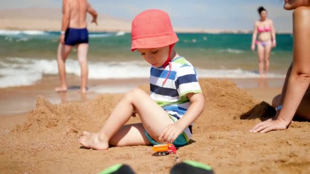 4k video de niño pequeño jugando con coche de juguete en la playa — Vídeos de Stock