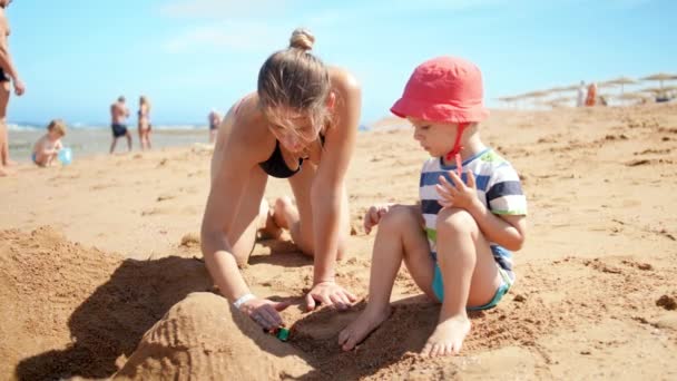 4K vídeo de menino pequeno brincando com sua mãe na praia ea. FAmily brincando de brinquedos e relaxando nas férias de verão — Vídeo de Stock